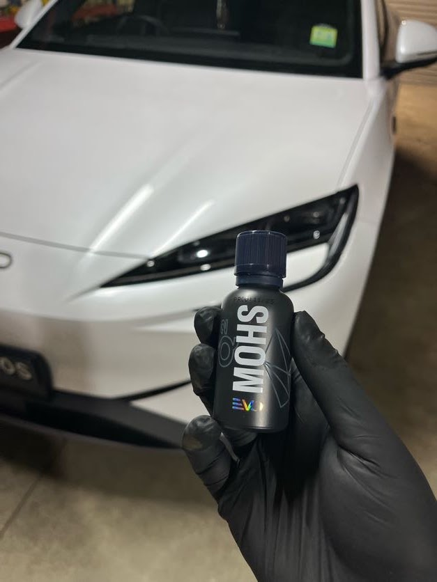 Gloved hand holding premium MOHS ceramic coating in front of a white luxury vehicle at Apex Detailing Cowandilla